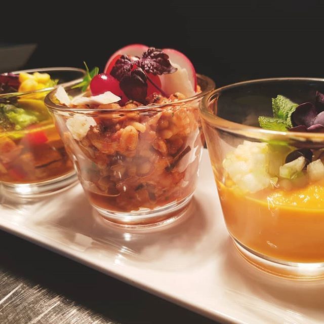 Drei farbenfrohe Vorspeisen in durchsichtigen Gläsern auf einem weißen Tablett