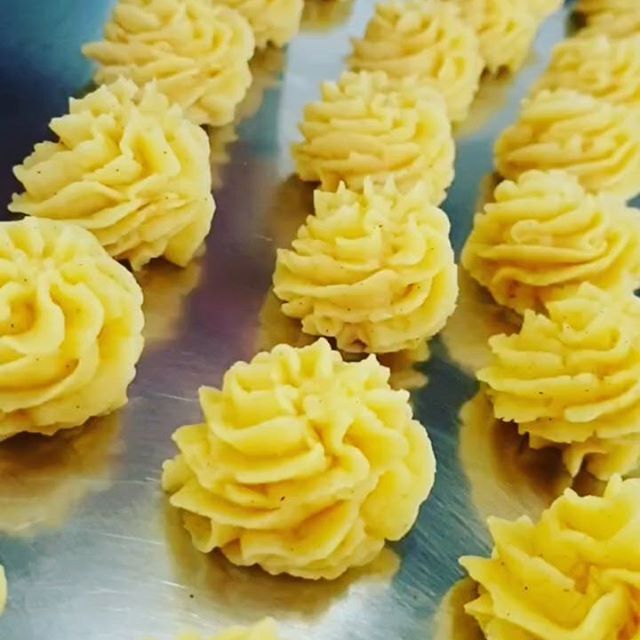 Reihen von aufgespritzten, goldgelben Kartoffelpüreestücken