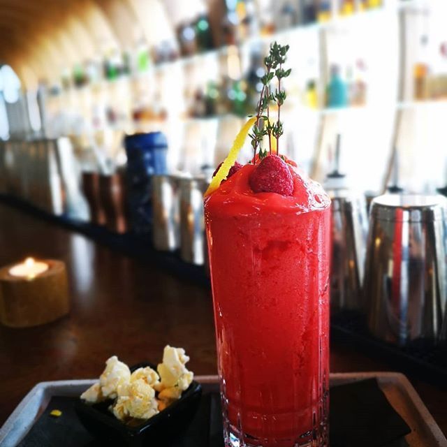 Ein roter Cocktail mit Garnitur steht auf einer Bar