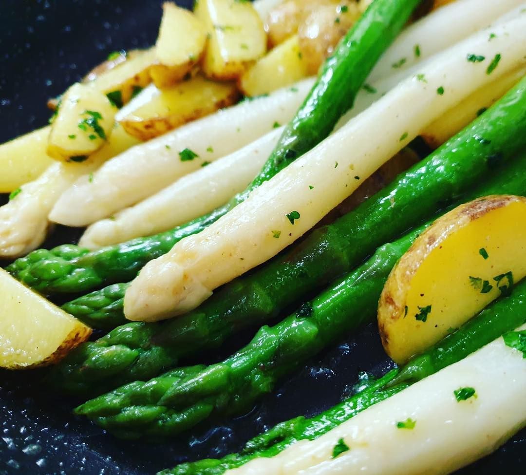 Grüner und weißer Spargel mit Bratkartoffeln, garniert mit Kräutern.