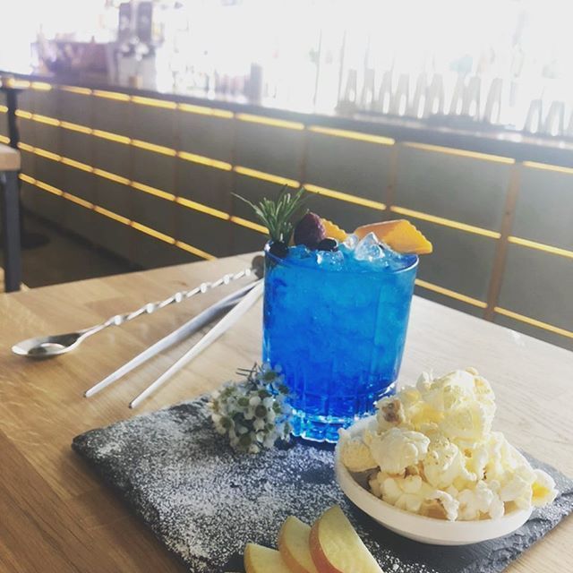 Blauer Cocktail mit Garnitur, Popcorn, Apfelscheiben und Barwerkzeugen