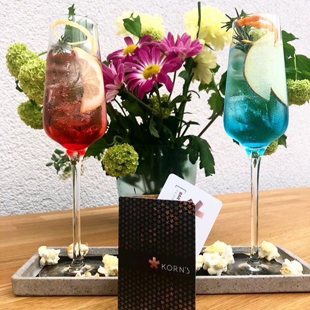 Zwei Cocktails, ein roter und ein blauer, dazu ein Blumenarrangement