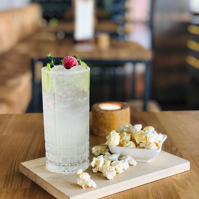 Cocktail mit Garnitur, Popcorn und Kerze auf einem Holzbrett