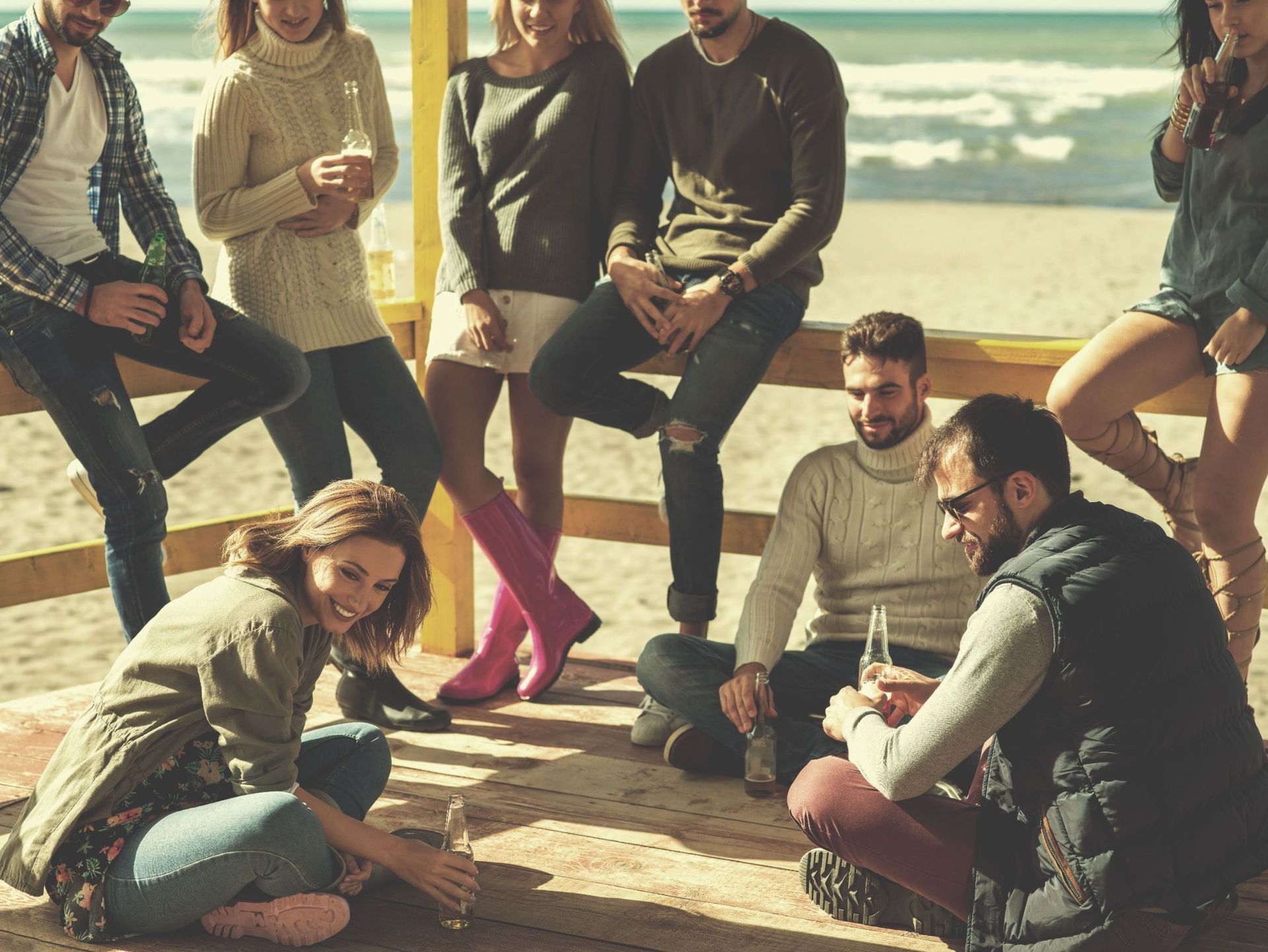 Un grupo de personas está sentada en una valla de madera en la playa.