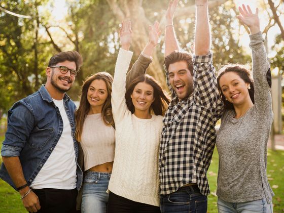 Un grupo de jóvenes está de pie en un parque con los brazos en el aire.