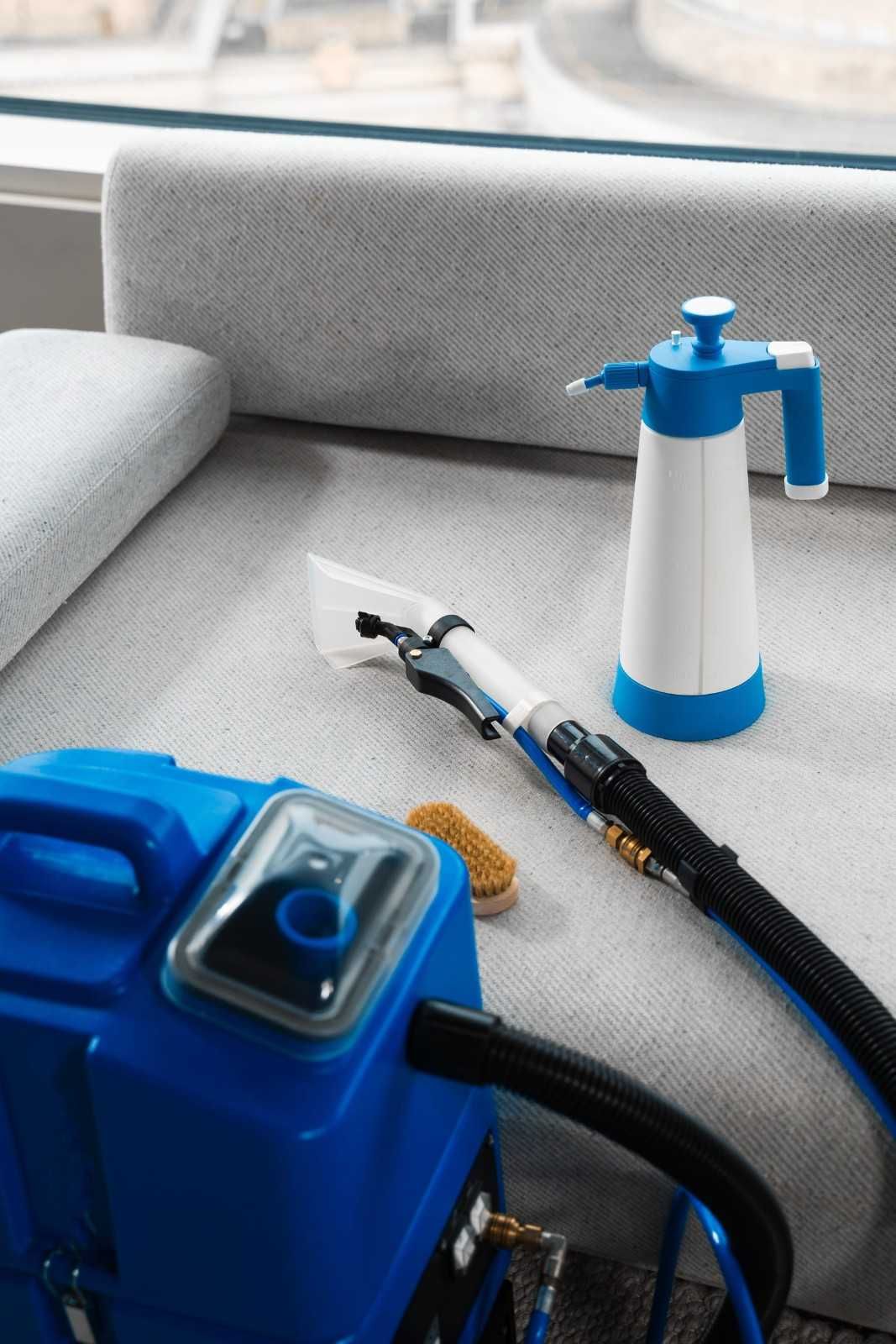 Bomba portátil azul y blanca con manguera y boquilla sobre un sofá gris junto a una ventana.