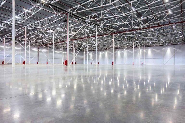 Nave industrial vacía con suelo de hormigón pulido y techo de cerchas metálicas.