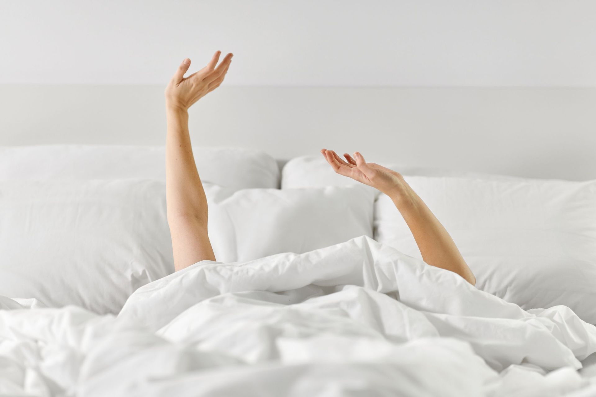 Una mujer está acostada en la cama con los brazos extendidos.