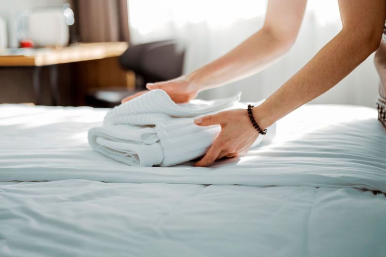 Una mujer está doblando toallas en una cama en una habitación de hotel.