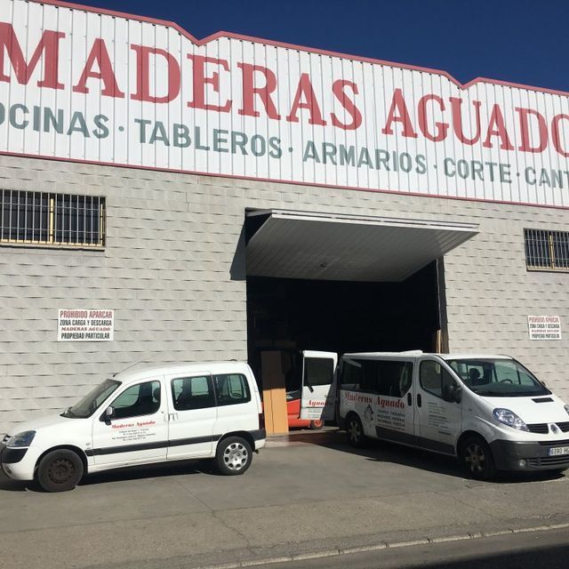 Dos camionetas blancas están estacionadas frente a un edificio que dice Maderas Aguado