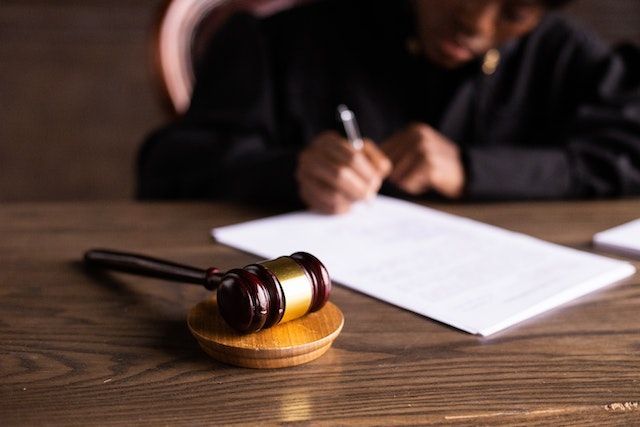 Un juez está escribiendo en un trozo de papel al lado de un mazo sobre una mesa de madera.