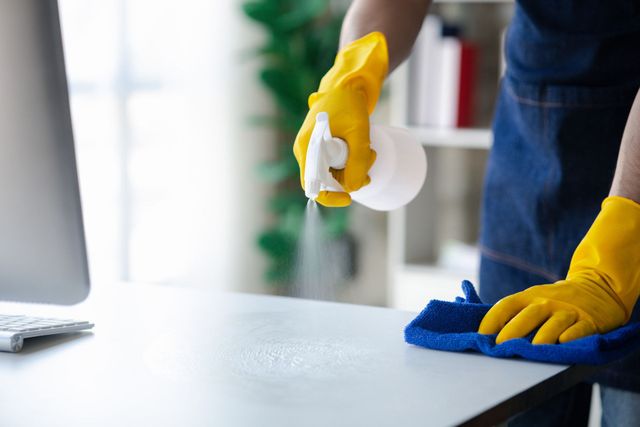 Una persona que lleva guantes amarillos está limpiando un escritorio frente a una computadora.