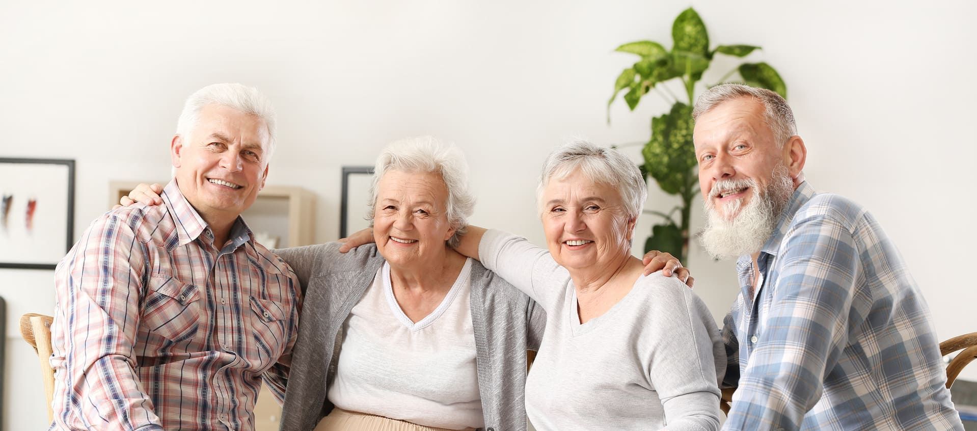 Eine Gruppe älterer Menschen posiert gemeinsam für ein Foto in einem Wohnzimmer.