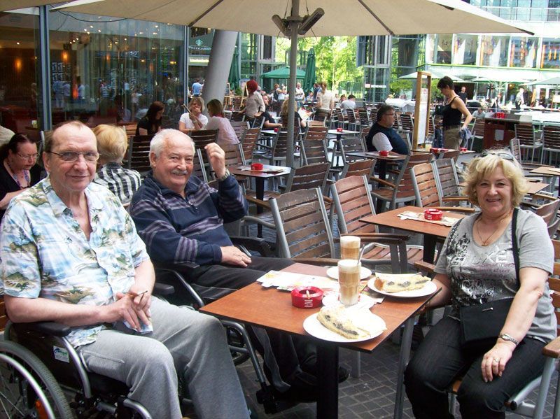Ein Mann im Rollstuhl sitzt mit zwei anderen Personen an einem Tisch