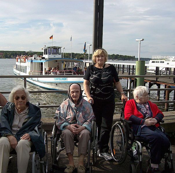 Eine Gruppe Rollstuhlfahrer posiert für ein Foto mit einem Boot im Hintergrund
