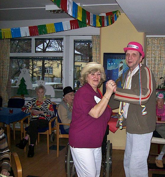 Ein Mann mit rosa Hut tanzt mit einer Frau im Rollstuhl