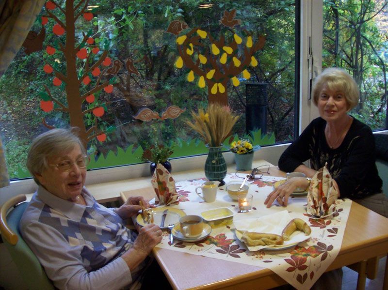 Zwei ältere Frauen sitzen mit Tellern voller Essen an einem Tisch
