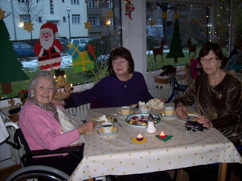 Eine Frau im Rollstuhl sitzt mit zwei anderen Frauen an einem Tisch