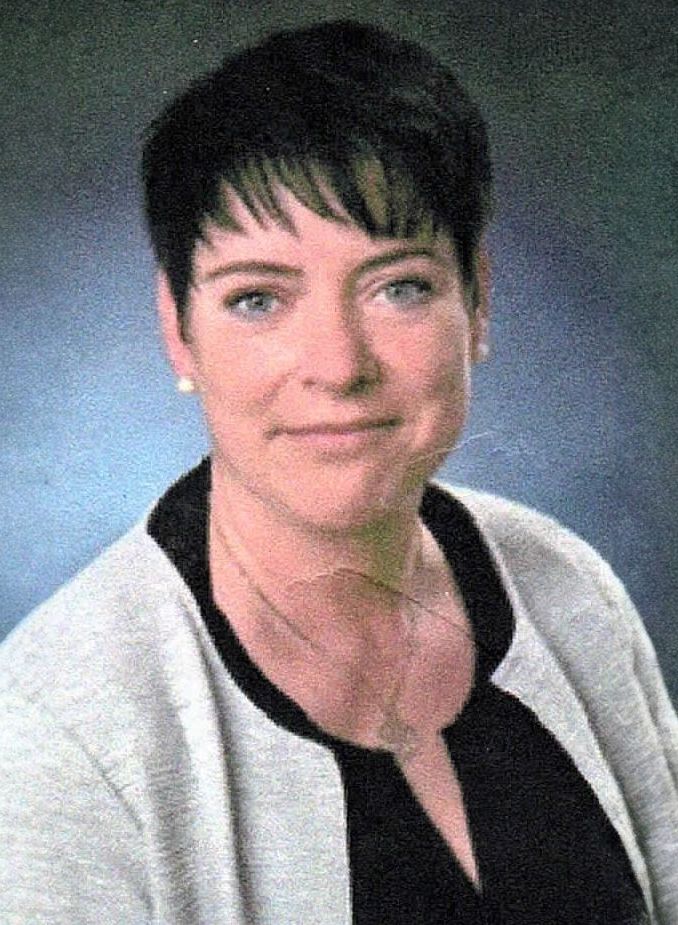 Eine Frau mit kurzen Haaren trägt einen grauen Pullover und ein schwarzes Hemd.