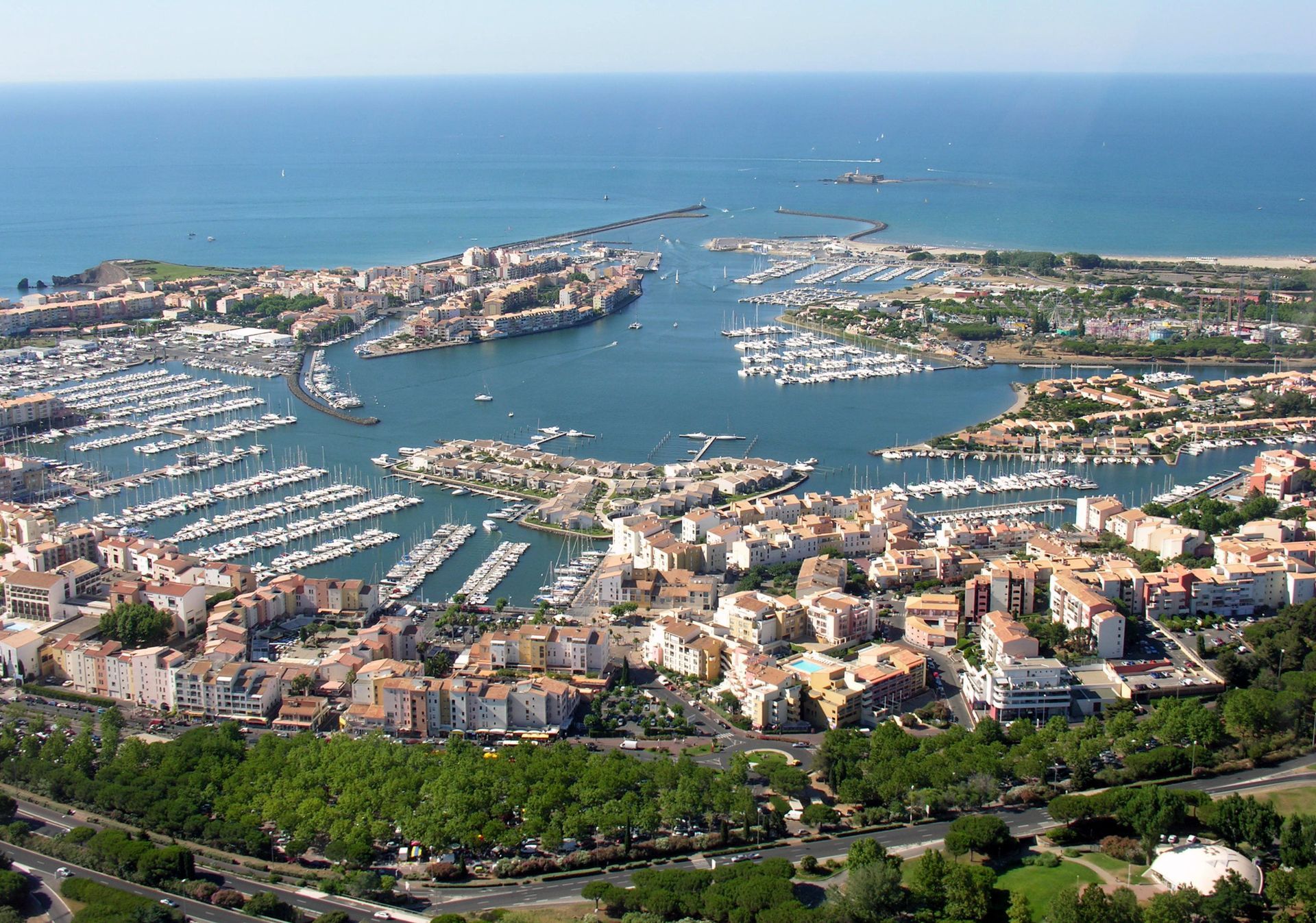 Vue aérienne d'une ville portuaire côtière avec des bateaux, une eau bleue et de nombreux bâtiments en bord de mer