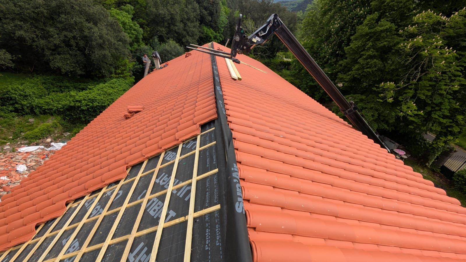 Ouvrier installant une toiture métallique rouge sur une charpente en bois