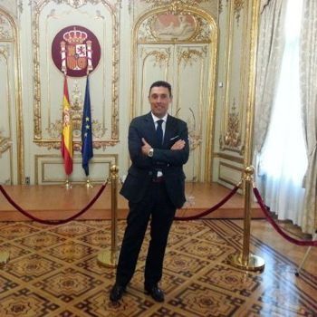 Un hombre con traje y corbata está de pie en una habitación con banderas en la pared.