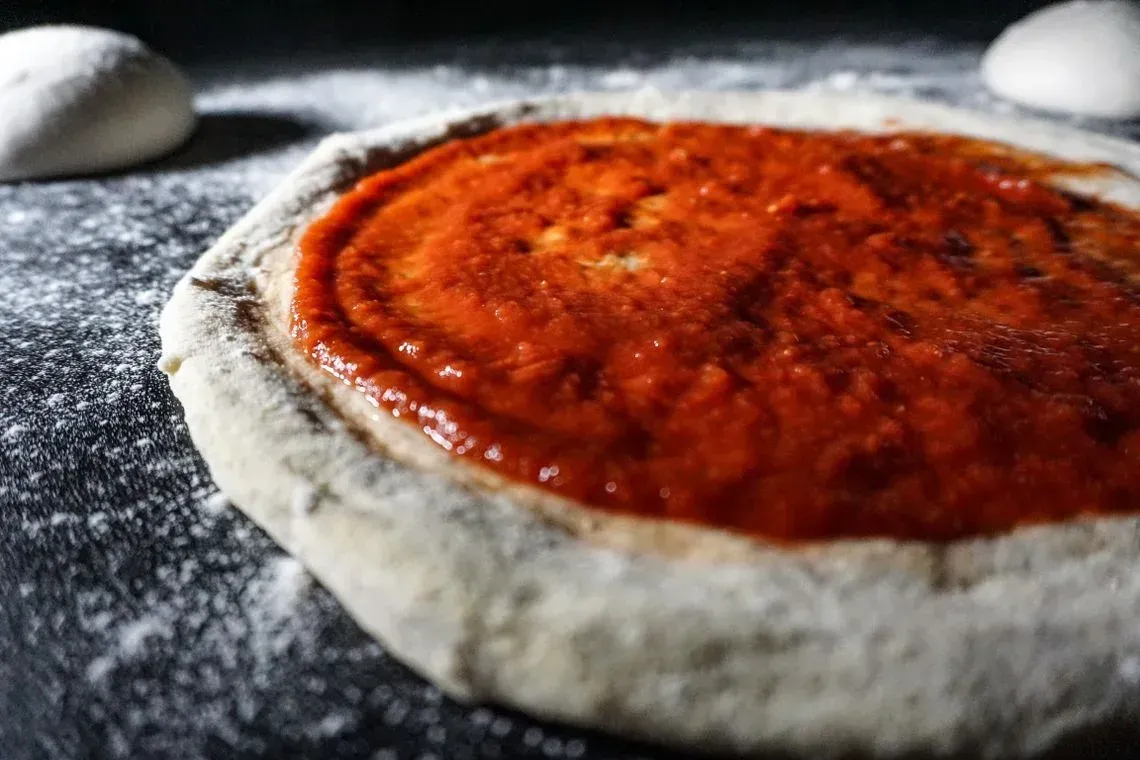Una pizza con salsa de tomate encima está sobre una mesa.