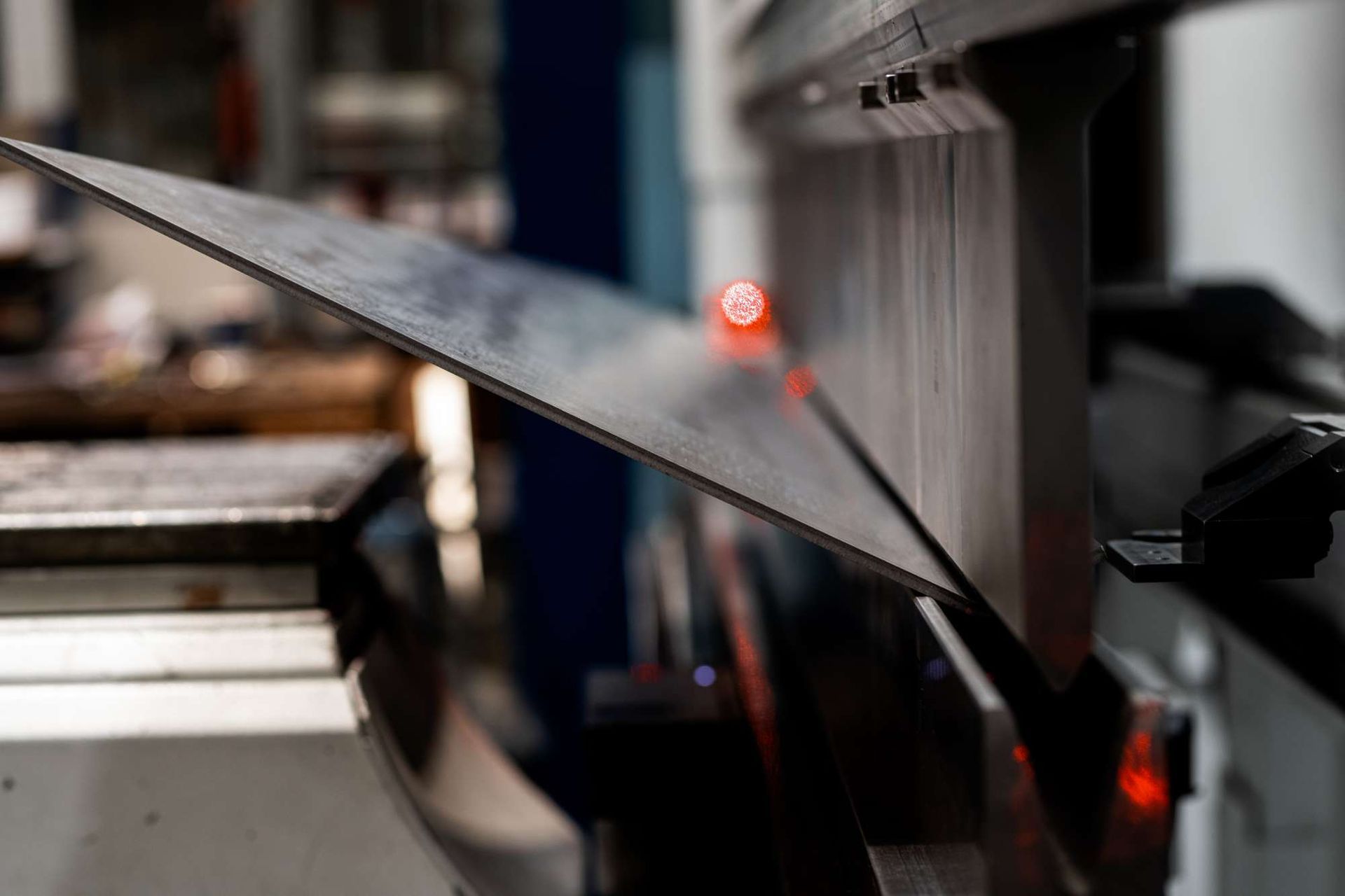 Metallblech wird von einer Maschine gebogen, rote Lichter zeigen den Biegepunkt an.