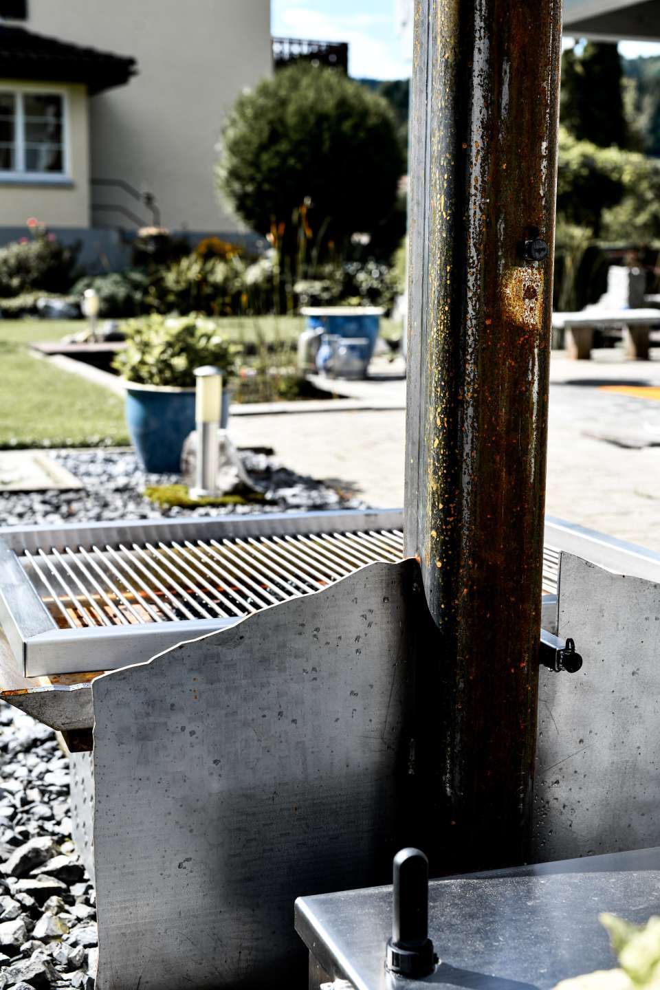 Außengrill mit verrostetem Metallpfosten in einem sonnigen Hinterhof.