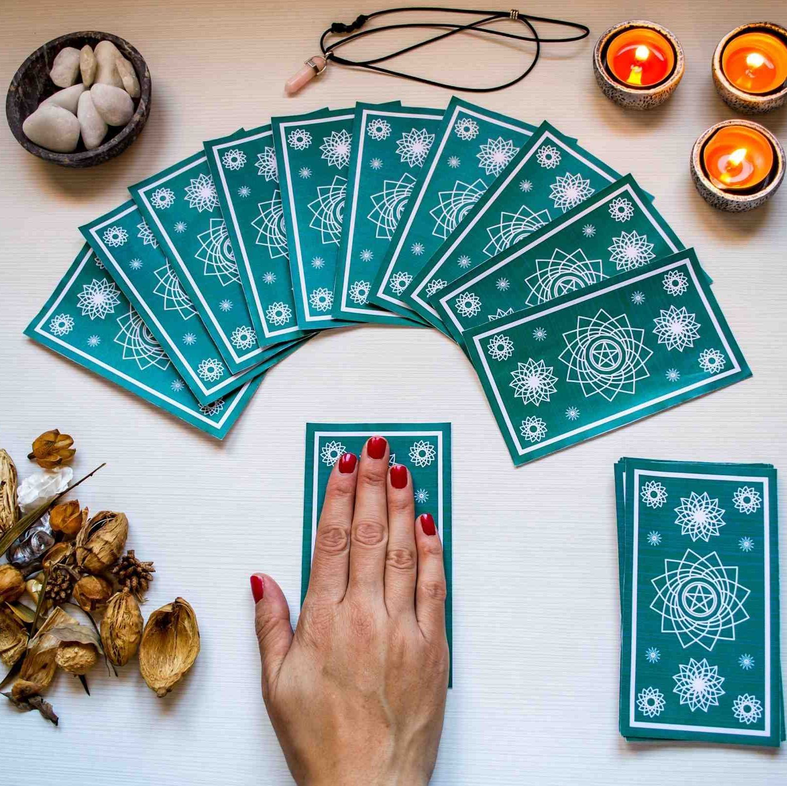 La mano de una mujer con uñas rojas está jugando cartas del tarot sobre una mesa.