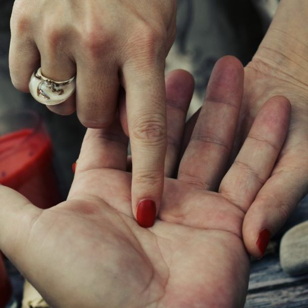 La mano de una mujer con uñas rojas y un anillo en el dedo.