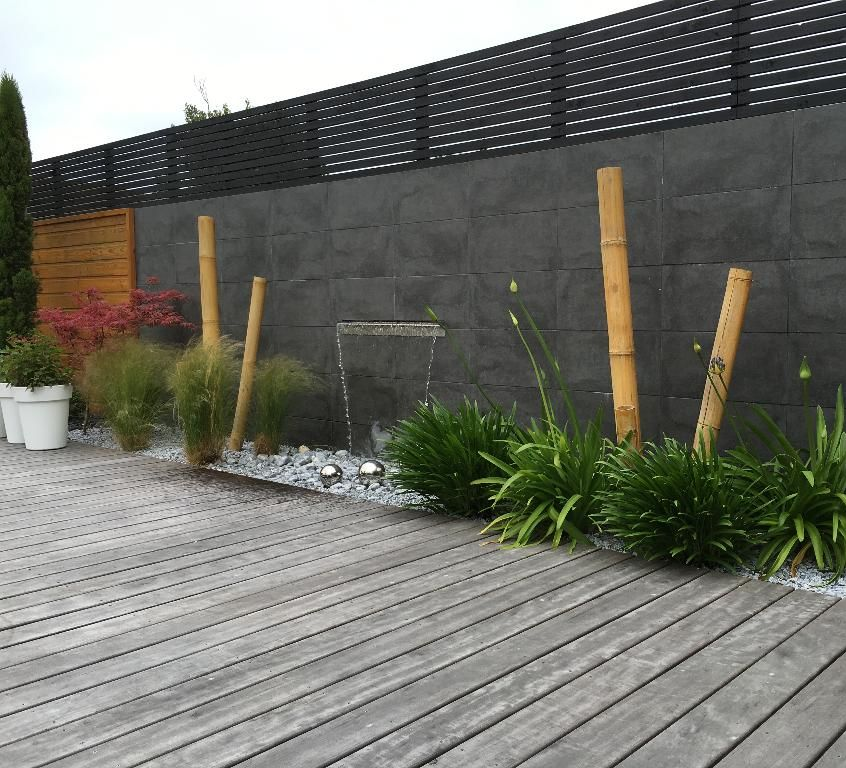 Terrasse en bois avec un mur en pierre sombre, des poteaux en bambou, une petite cascade et un aménagement paysager.