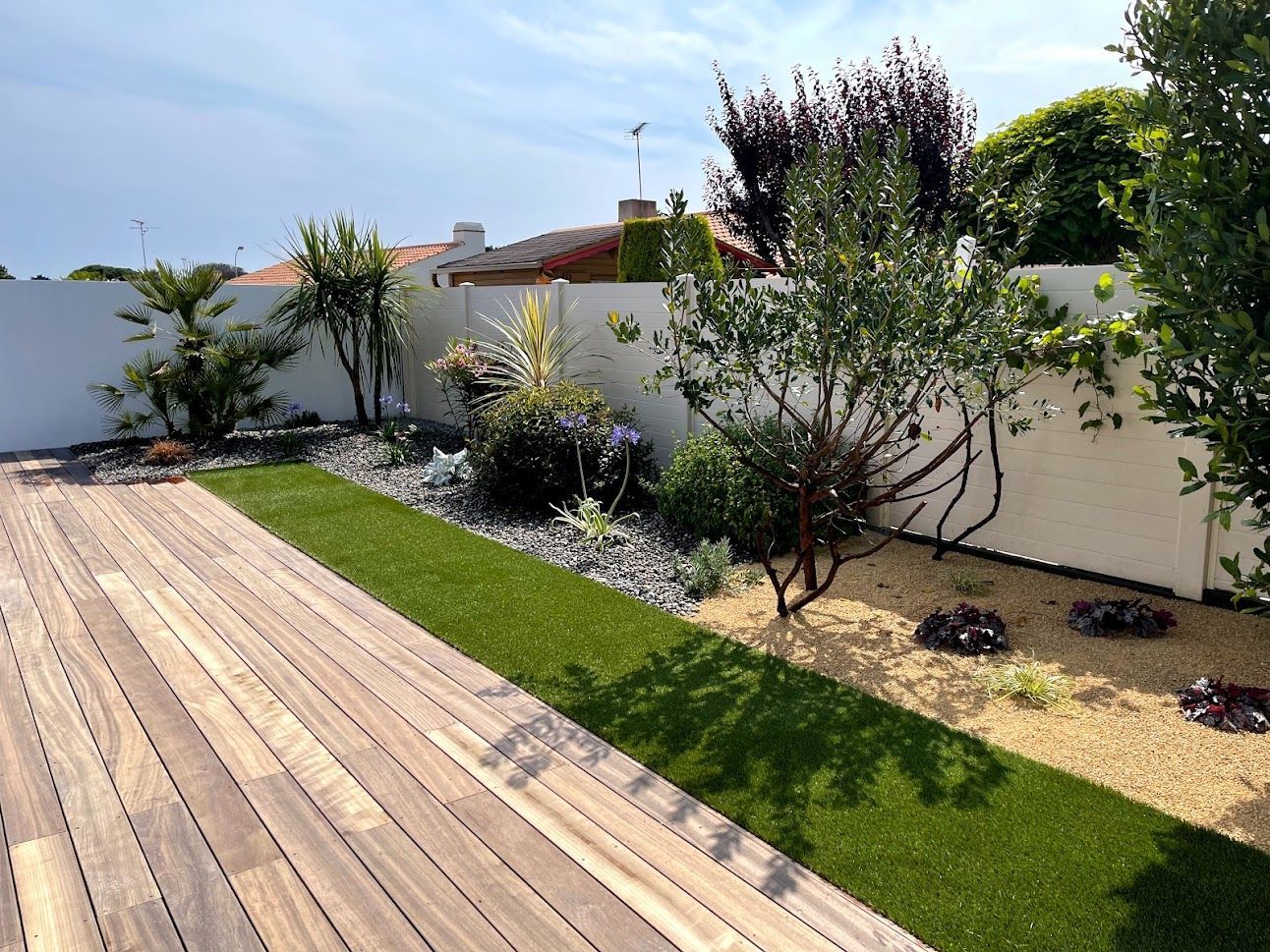 Un jardin paysager avec un palmier, une couverture de piscine et des parterres de gravier bordés d'une clôture gris foncé.