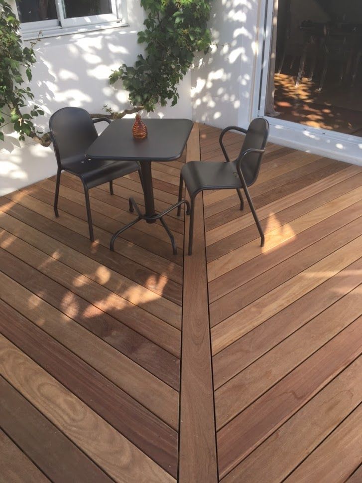 Terrasse en bois devant une maison, avec des planches brun rougeâtre. Jardin nu en arrière-plan.