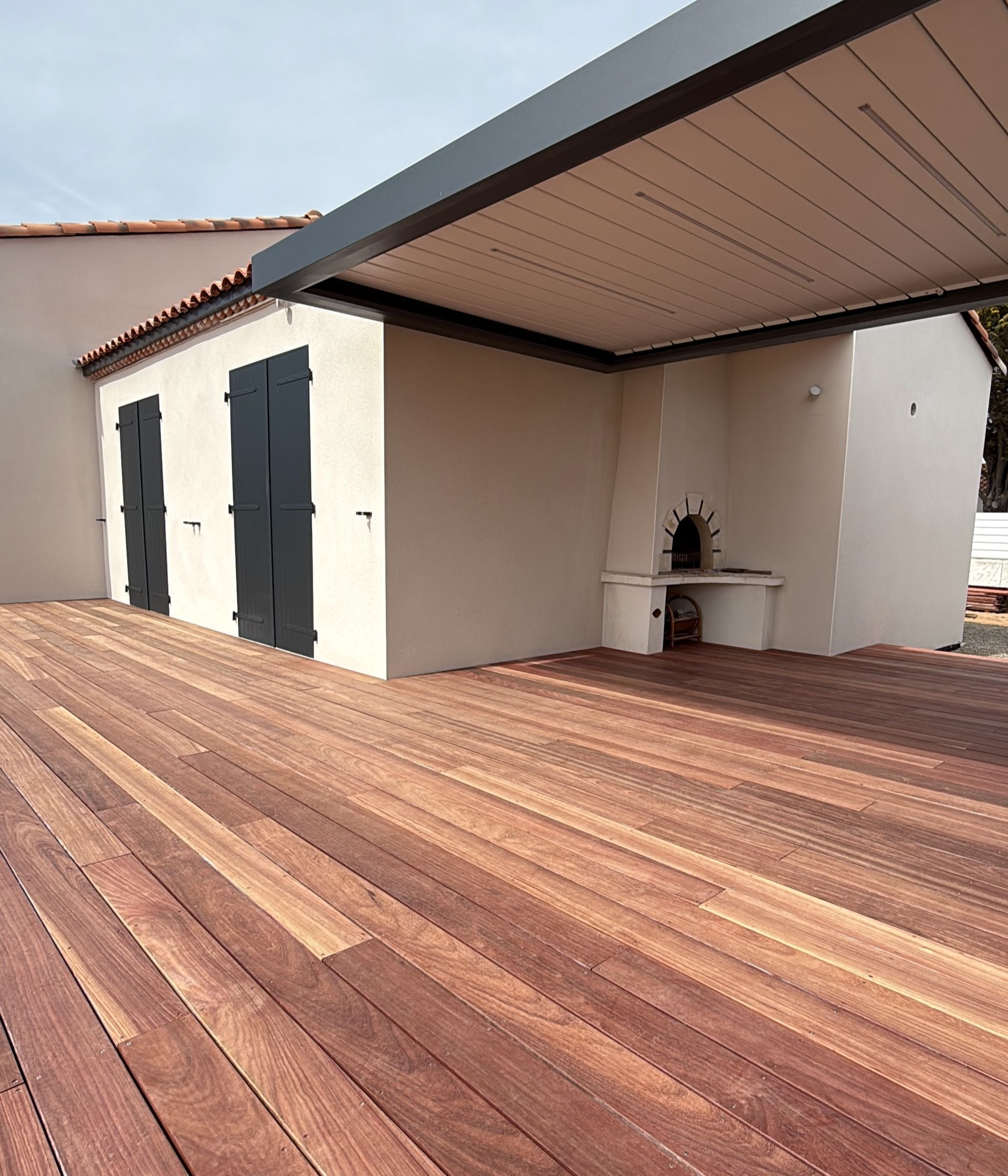Terrasse en bois avec un bâtiment doté de volets noirs et d'une cheminée extérieure.