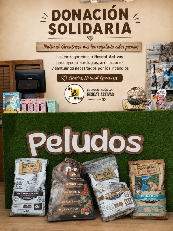 Exhibición de donación de comida para mascotas españolas con letrero de “Donación Solidaria” y bolsas de comida para perros Peludos sobre una mesa verde.