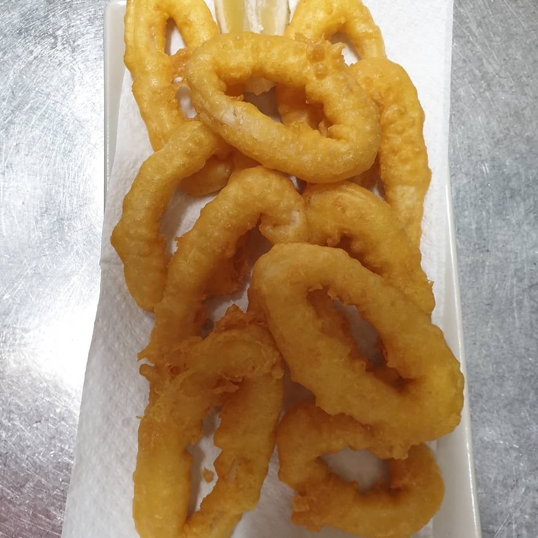 Un plato blanco cubierto con aros de cebolla fritos sobre una toalla de papel.