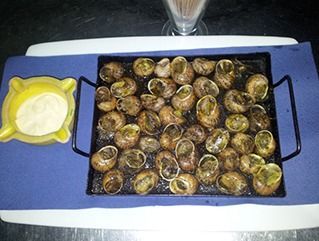 Una bandeja de caracoles en una mesa junto a un cenicero.