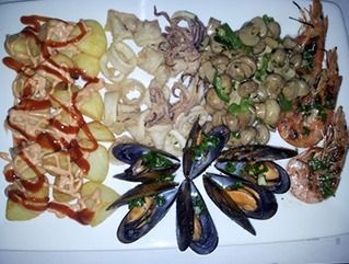 Un plato blanco cubierto con una variedad de mariscos y patatas.