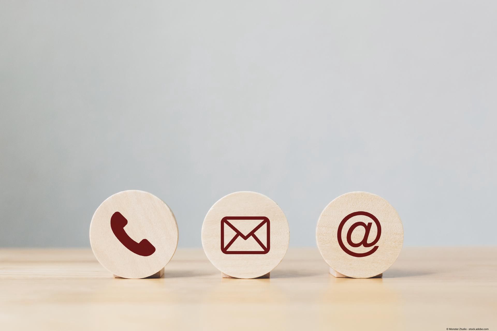 Drei runde Holzscheiben mit dunkelroten Symbolen für Telefon, E-Mail und E-Mail-Adresse nebeneinander auf hellem Untergrund.