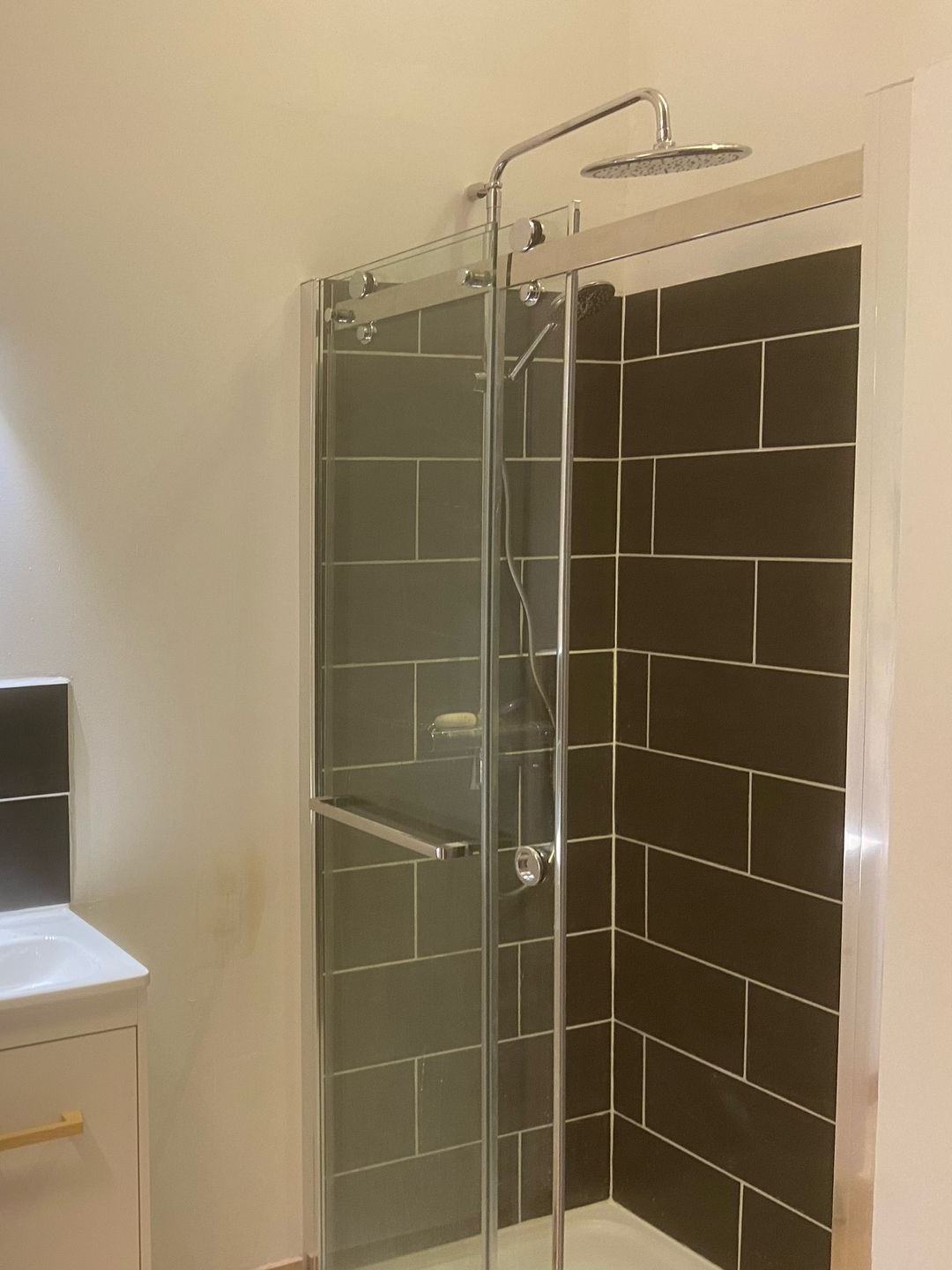 Cabine de douche avec murs carrelés marron et porte vitrée.