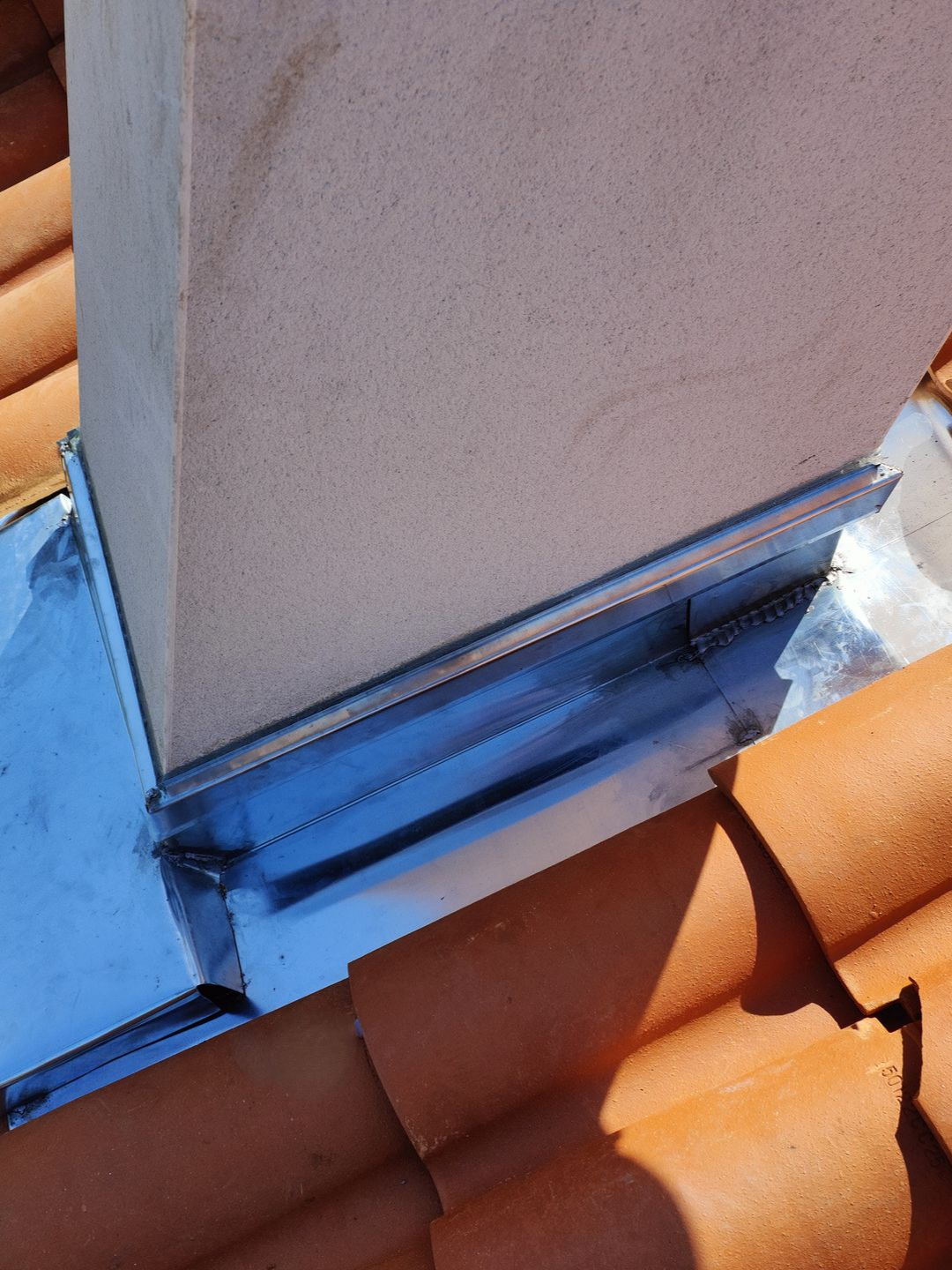 Solin en plomb autour d'une cheminée sur un toit en tuiles en terre cuite.