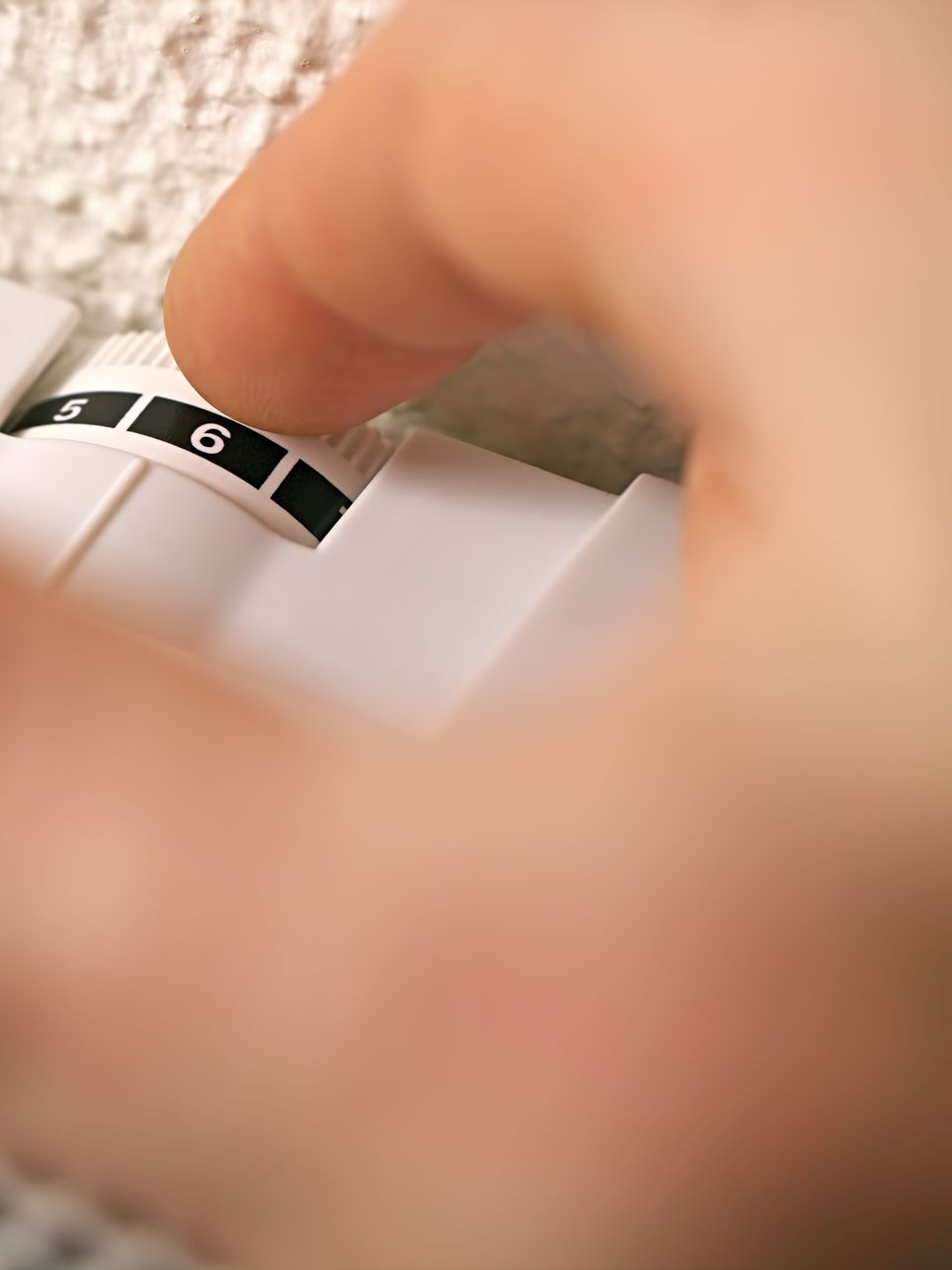 Une main réglant un cadran de thermostat blanc, le faisant passer de 5 à 6.