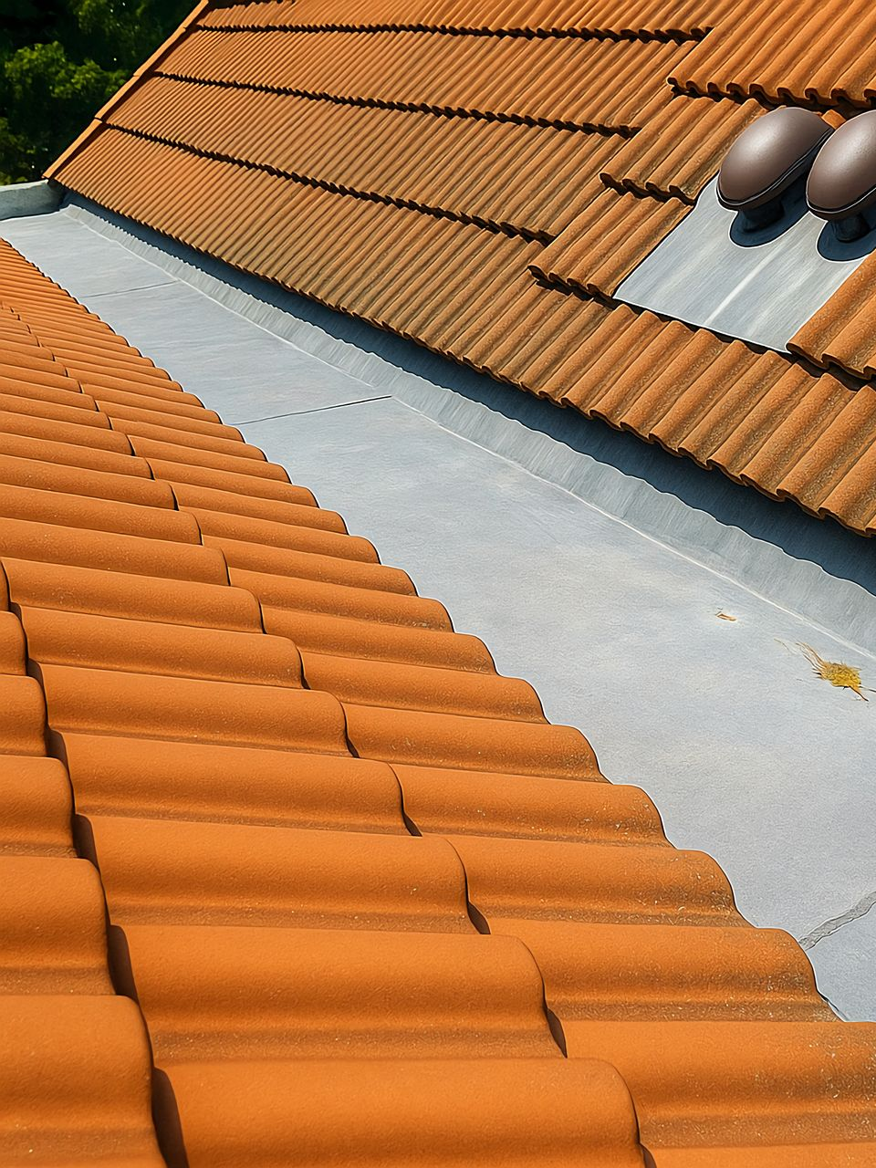 Toiture en tuiles orange avec solin gris, près d'un évent brun foncé.