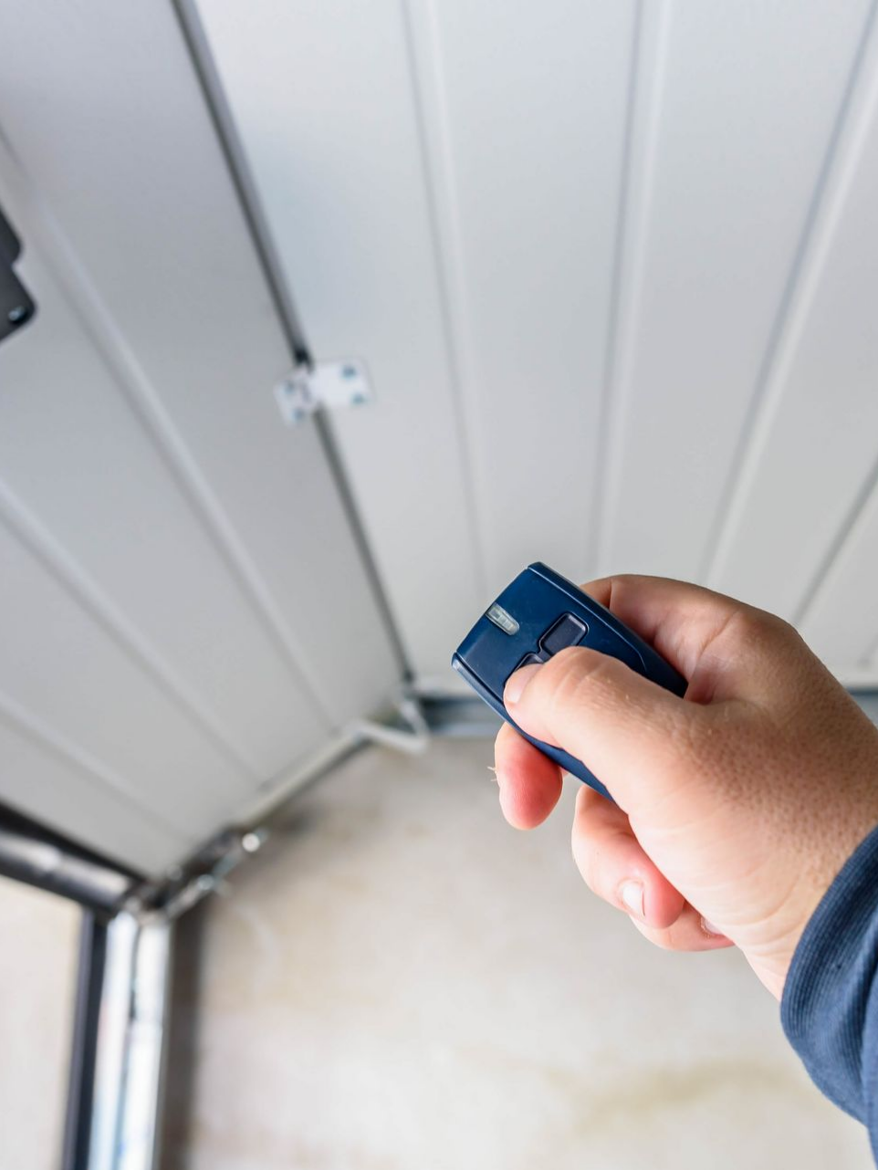 Main tenant un ouvre-porte de garage bleu, ouvrant la porte de garage blanche.