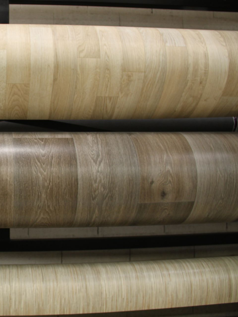 Rouleaux de revêtement de sol en vinyle aux motifs de grain de bois clair et moyen, empilés sur des présentoirs.