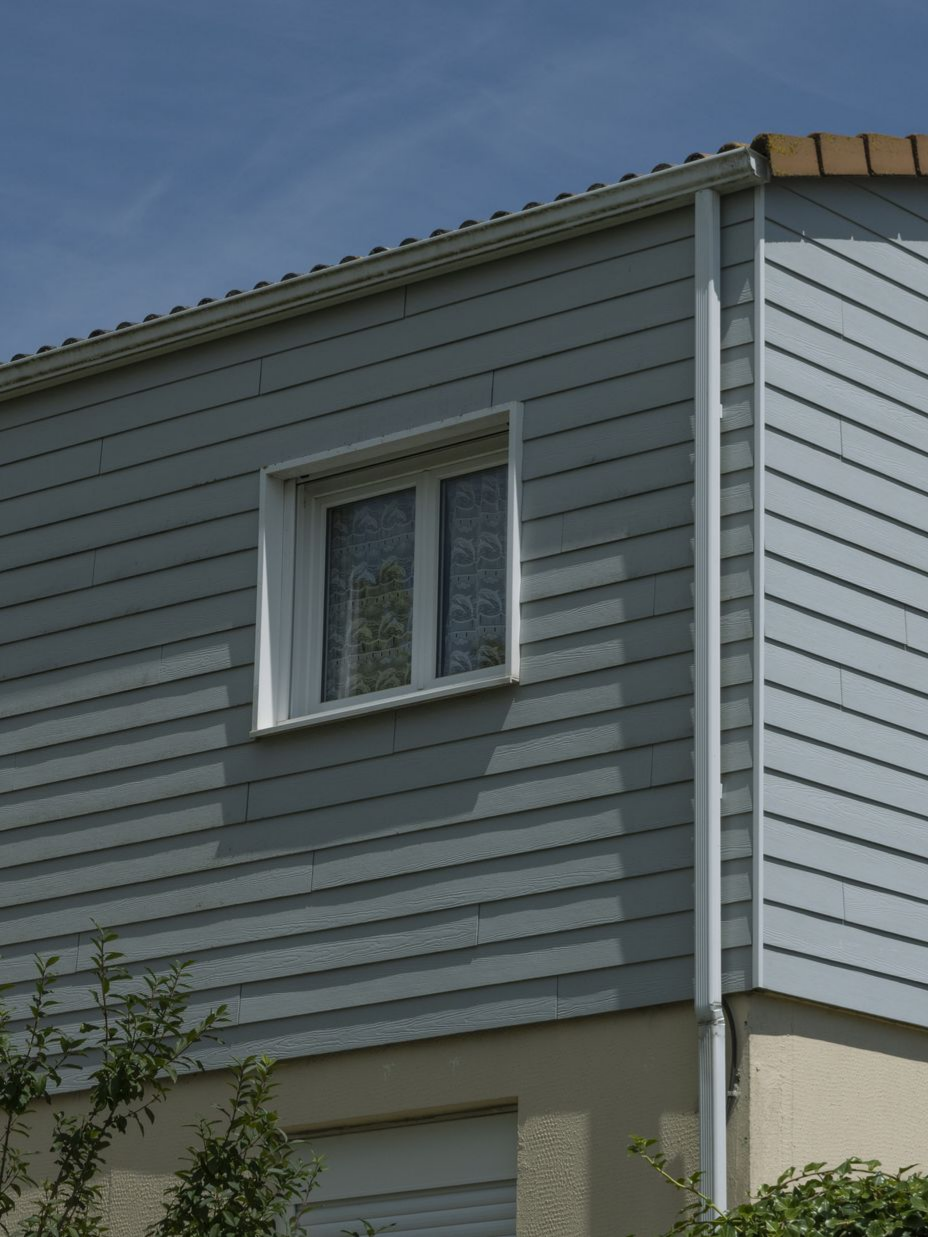 Revêtement gris avec garniture blanche autour d'une fenêtre et d'un tuyau de descente sur une maison.