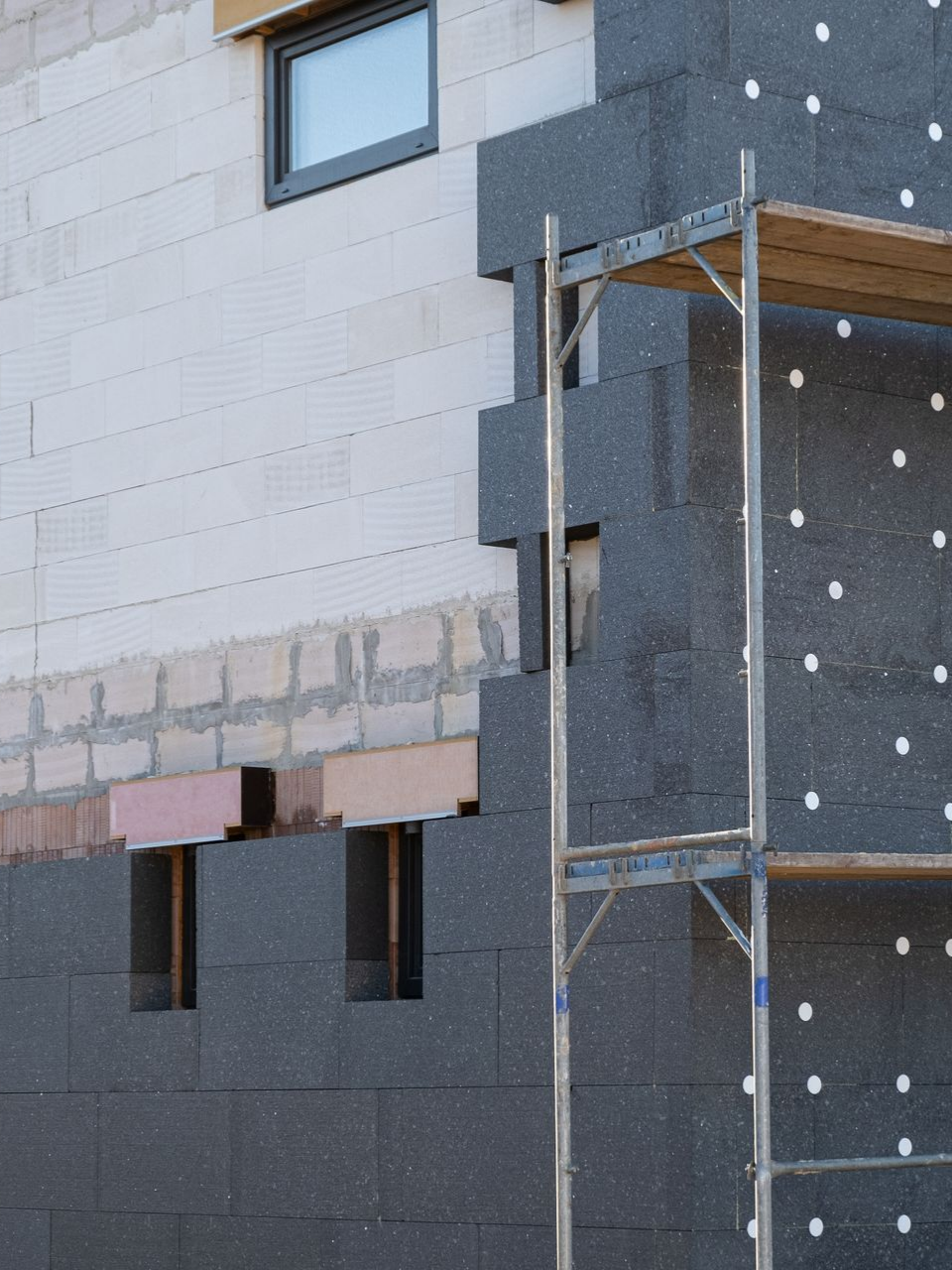Extérieur du bâtiment avec panneaux isolants foncés en cours d'installation et échafaudage.