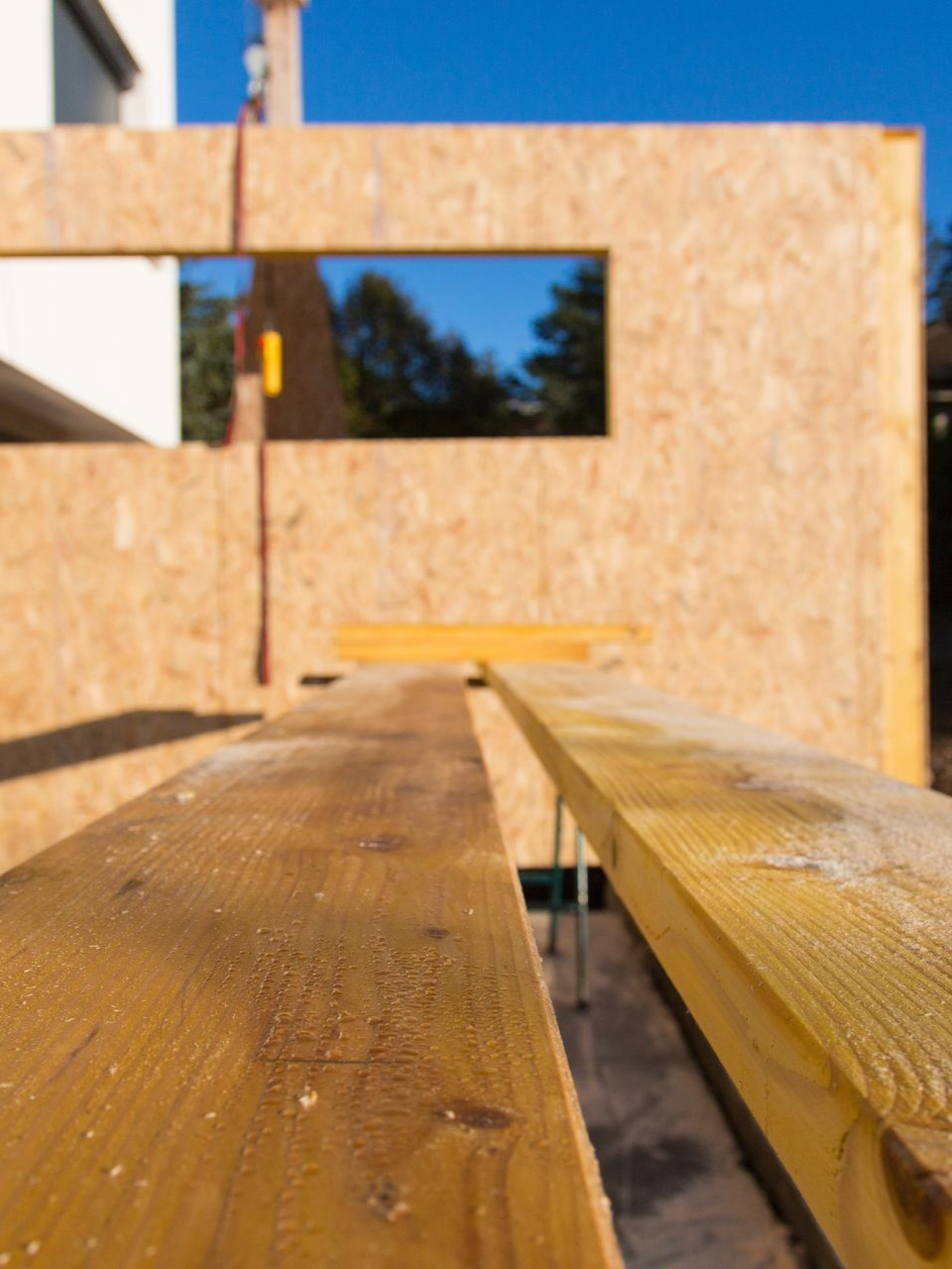 Chantier de construction axé sur les planches de bois, le mur OSB et le cadre de fenêtre, ciel bleu.