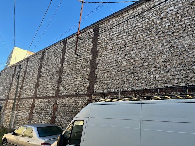 Une camionnette et une voiture blanches garées près d'un bâtiment en briques orné de bandes verticales sombres. Des fils électriques sont suspendus au-dessus.